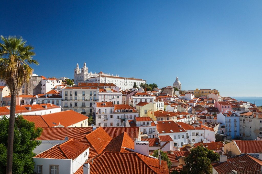 A city shot of white houses with red roofs in Portugal. The sky is bright blue and cloudless.